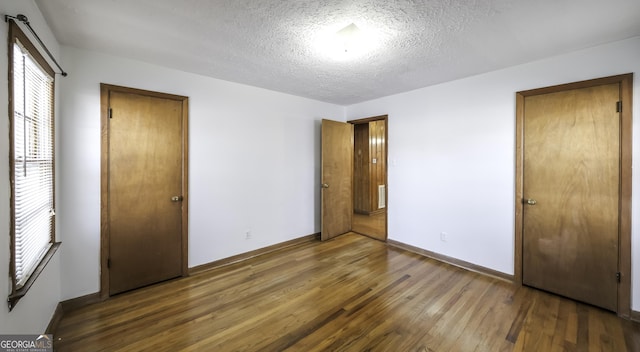 unfurnished bedroom with a textured ceiling and dark wood-type flooring