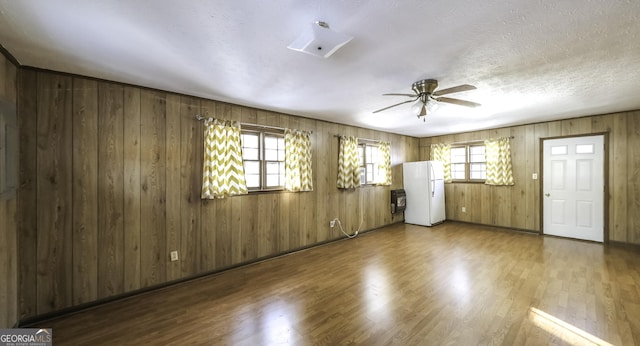 unfurnished room with ceiling fan, wood walls, wood-type flooring, and a textured ceiling