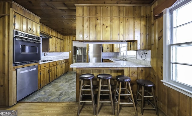 kitchen featuring wood walls, wooden ceiling, sink, appliances with stainless steel finishes, and kitchen peninsula