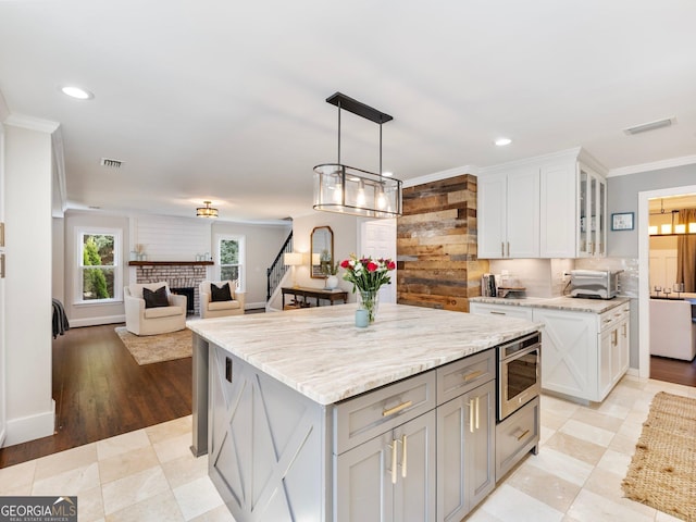 kitchen featuring crown molding, a center island, pendant lighting, a fireplace, and white cabinets