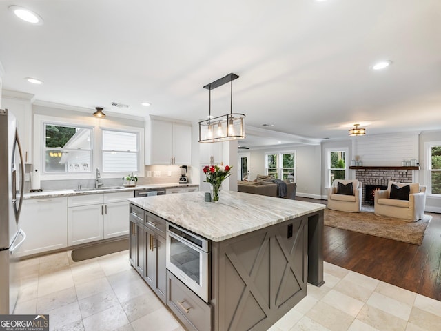 kitchen with stainless steel appliances, a sink, white cabinetry, a center island, and pendant lighting