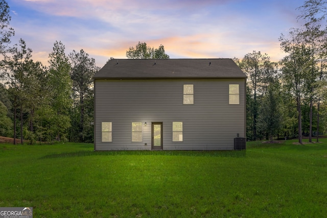 back house at dusk featuring a lawn and central AC unit