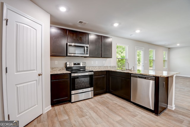 kitchen with sink, light wood-type flooring, light stone countertops, appliances with stainless steel finishes, and kitchen peninsula