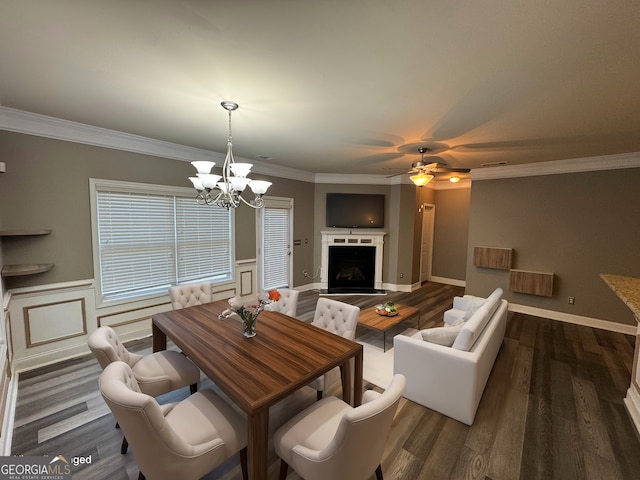 dining space with dark wood-type flooring, ceiling fan with notable chandelier, and crown molding