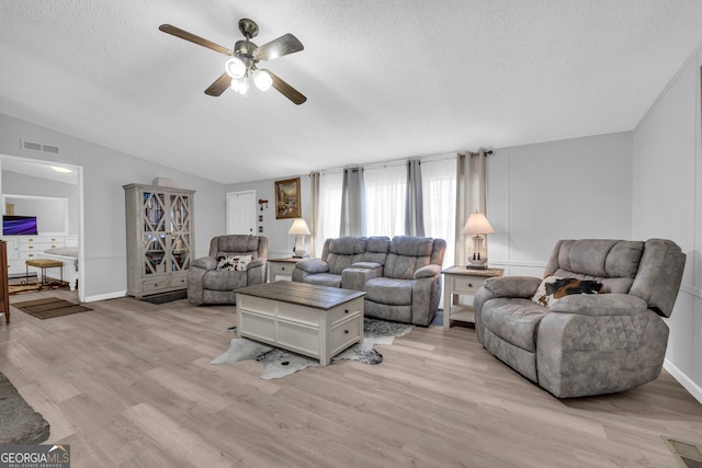 living room featuring a textured ceiling, light wood-type flooring, ceiling fan, and lofted ceiling