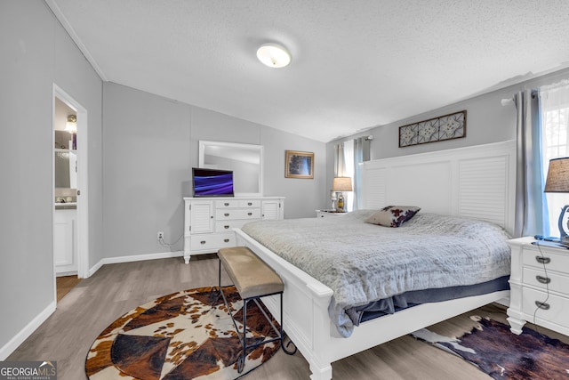 bedroom with wood-type flooring, a textured ceiling, ensuite bathroom, and lofted ceiling