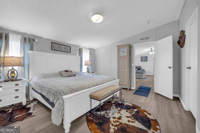 bedroom featuring a textured ceiling, light hardwood / wood-style flooring, and vaulted ceiling