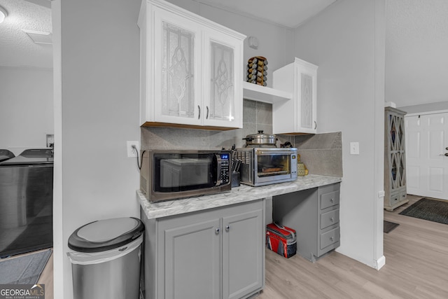 kitchen featuring light wood-type flooring, tasteful backsplash, a textured ceiling, gray cabinets, and washer / clothes dryer