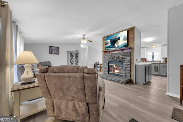 living room with light wood-type flooring, a textured ceiling, vaulted ceiling, ceiling fan, and a fireplace