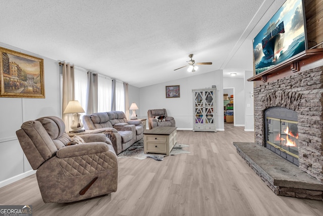 living room featuring a stone fireplace, vaulted ceiling, ceiling fan, light wood-type flooring, and a textured ceiling