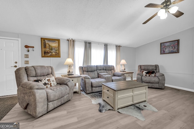 living room with ceiling fan, light wood-type flooring, a textured ceiling, and vaulted ceiling