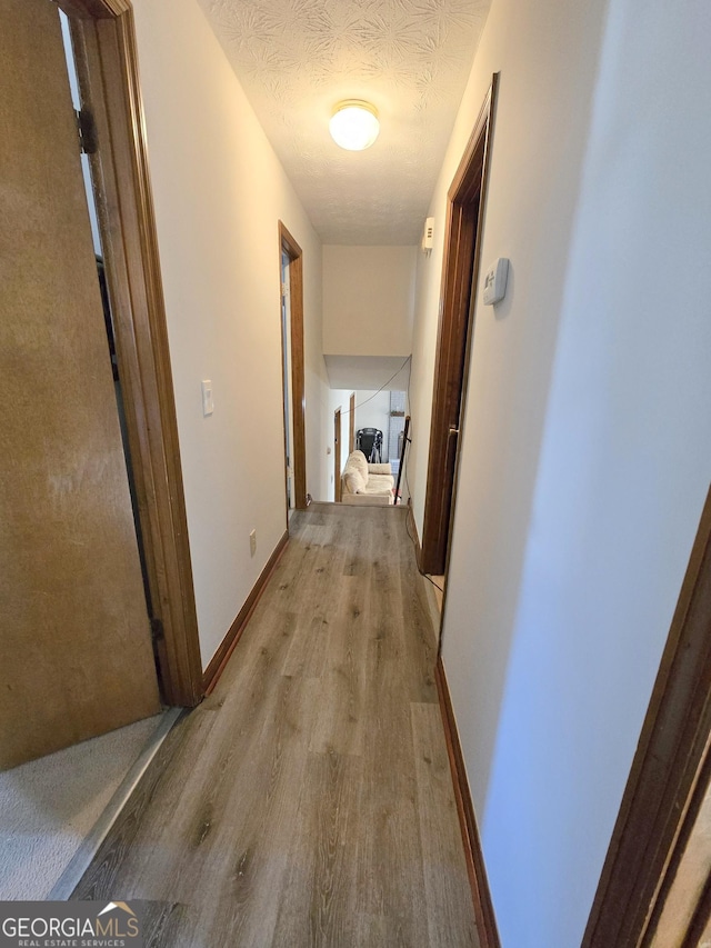 corridor with a textured ceiling and light hardwood / wood-style flooring