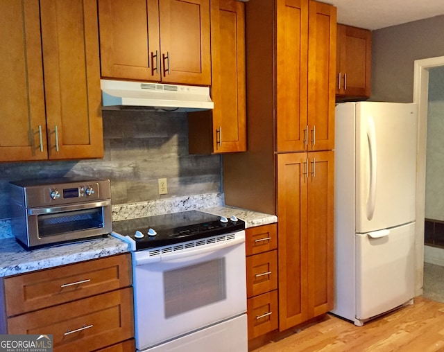 kitchen with backsplash, light stone counters, light hardwood / wood-style floors, and white appliances