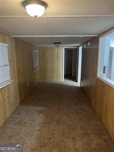 empty room featuring a textured ceiling, wooden walls, and carpet flooring