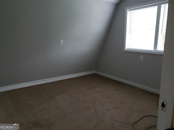 spare room featuring carpet and vaulted ceiling