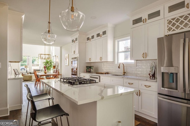 kitchen featuring stainless steel appliances, sink, white cabinetry, a kitchen island, and hanging light fixtures