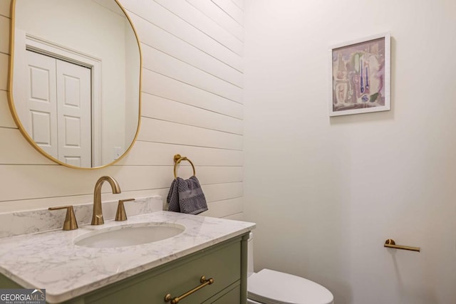 bathroom with vanity, wood walls, and toilet