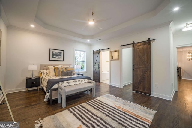 bedroom featuring ensuite bath, a raised ceiling, ceiling fan, dark wood-type flooring, and a barn door