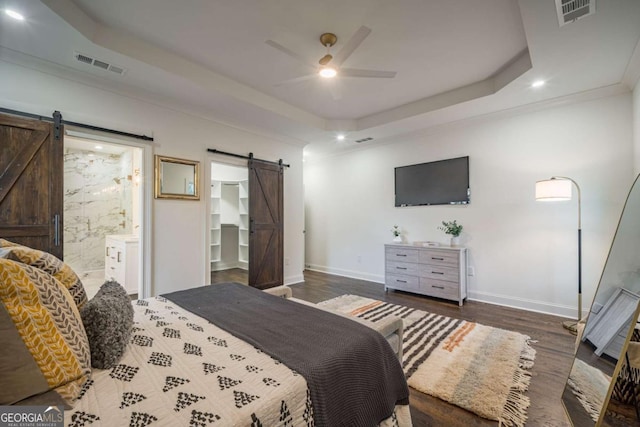 bedroom featuring ceiling fan, dark hardwood / wood-style floors, a barn door, connected bathroom, and a tray ceiling