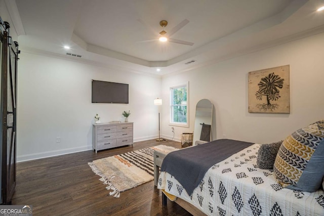 bedroom with dark wood-type flooring, crown molding, ceiling fan, a barn door, and a tray ceiling