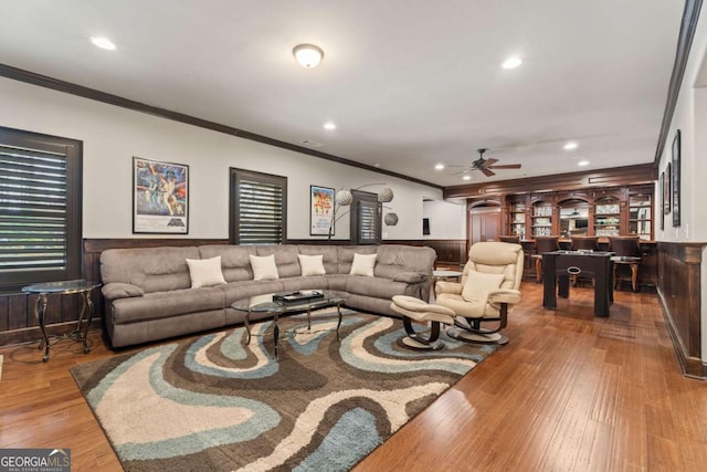 living room with ceiling fan, wood walls, light hardwood / wood-style floors, and crown molding