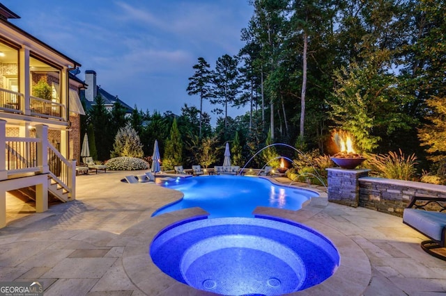 pool at dusk with an in ground hot tub, pool water feature, and a patio