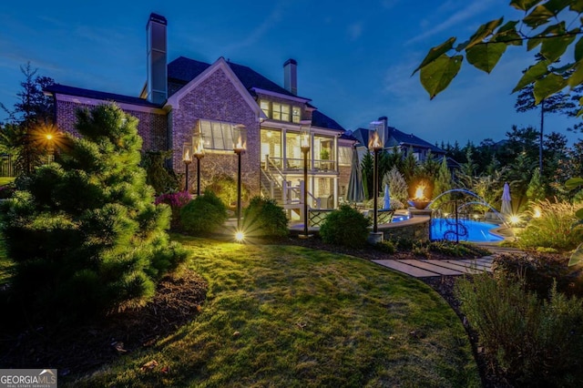 back house at dusk featuring a lawn and a sunroom