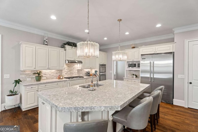 kitchen featuring built in appliances, white cabinets, sink, and an island with sink