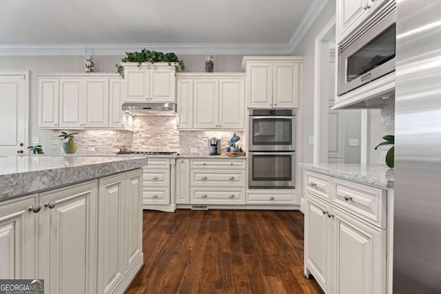 kitchen with light stone countertops, stainless steel appliances, tasteful backsplash, white cabinets, and ornamental molding