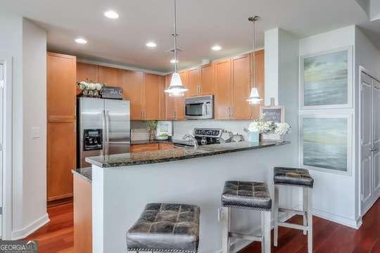 kitchen with kitchen peninsula, appliances with stainless steel finishes, dark stone counters, dark wood-type flooring, and pendant lighting