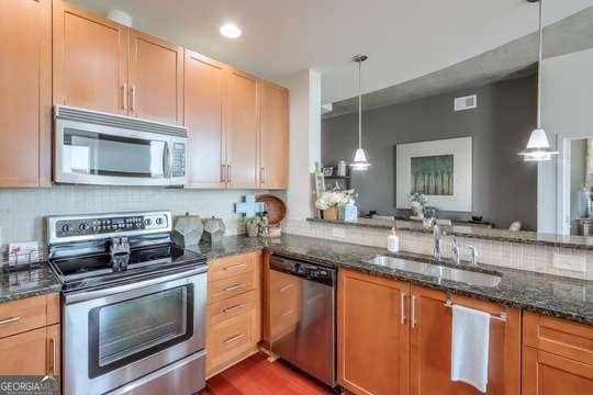 kitchen with decorative light fixtures, stainless steel appliances, and dark stone counters