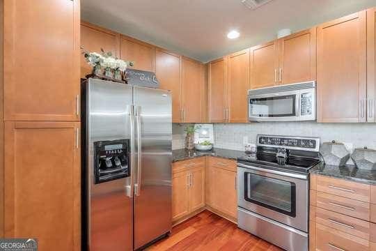 kitchen featuring light brown cabinets, stainless steel appliances, light hardwood / wood-style flooring, and dark stone countertops