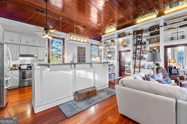 living room featuring ceiling fan, built in features, hardwood / wood-style floors, and wooden ceiling