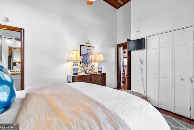 bedroom with connected bathroom, ceiling fan, dark wood-type flooring, high vaulted ceiling, and a closet