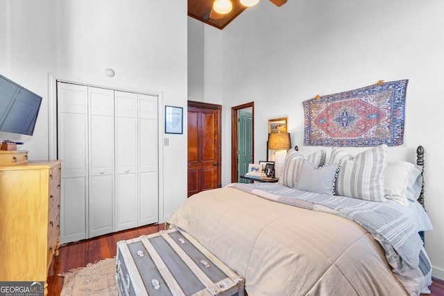 bedroom with a closet, ceiling fan, dark hardwood / wood-style flooring, and a high ceiling