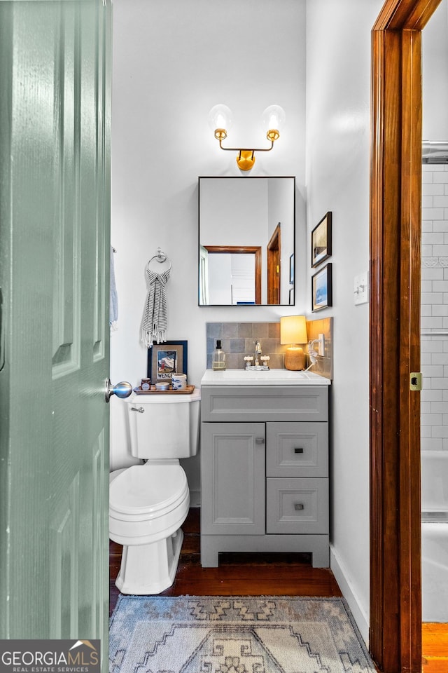 bathroom featuring hardwood / wood-style floors, decorative backsplash, toilet, and vanity