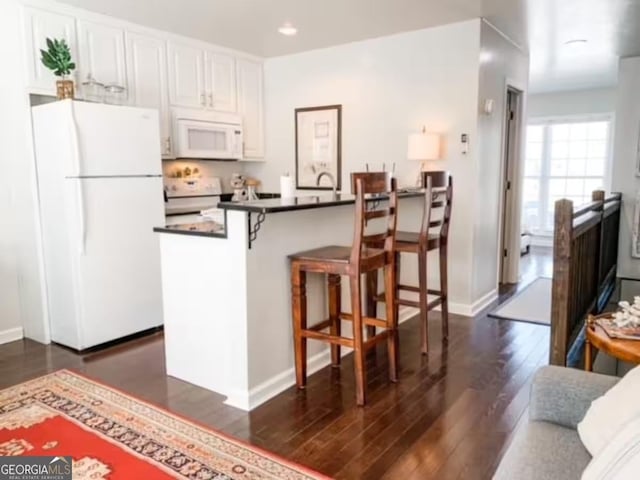 kitchen featuring white appliances, dark wood-type flooring, white cabinets, kitchen peninsula, and a breakfast bar area