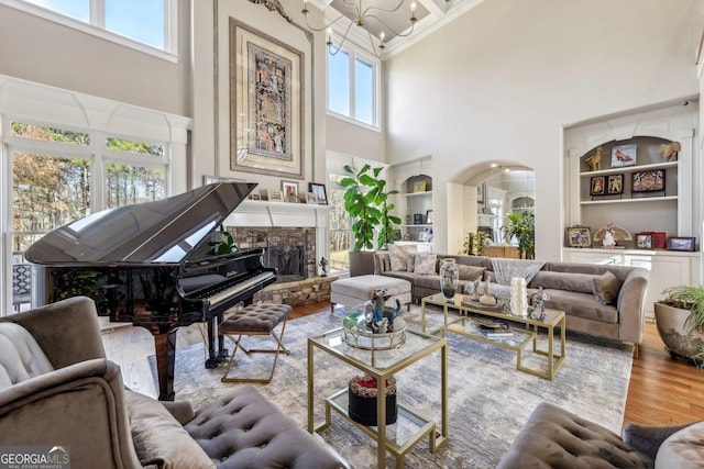 sitting room with built in features, a notable chandelier, a fireplace, light hardwood / wood-style floors, and a high ceiling