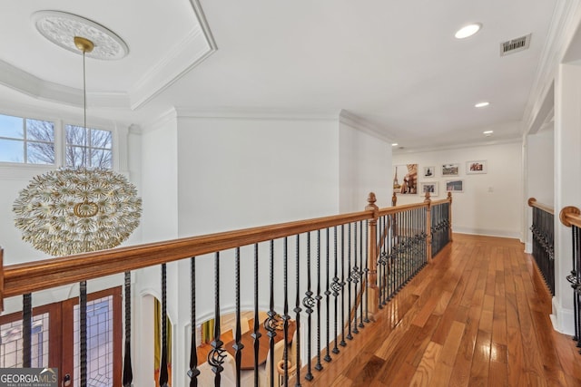 hallway with hardwood / wood-style flooring, crown molding, a raised ceiling, and a notable chandelier