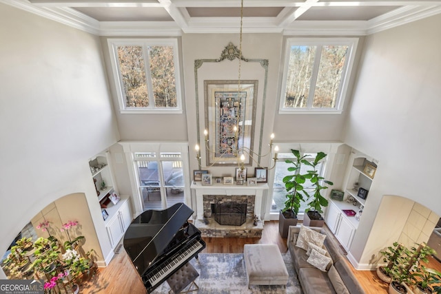 living room featuring hardwood / wood-style flooring, a towering ceiling, coffered ceiling, and a stone fireplace