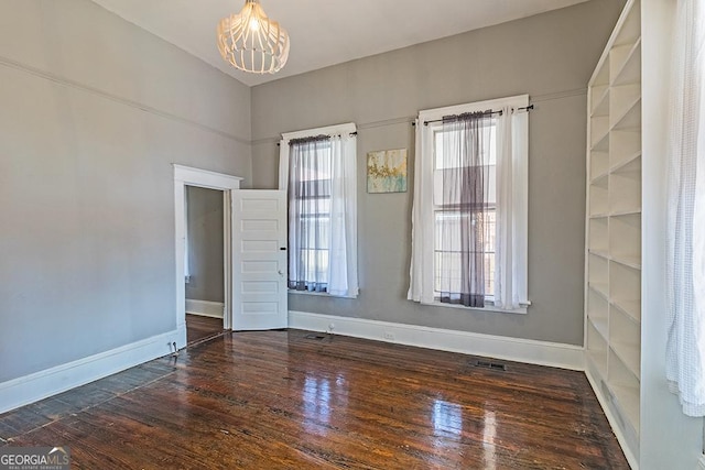 unfurnished room with an inviting chandelier, a healthy amount of sunlight, and dark hardwood / wood-style floors