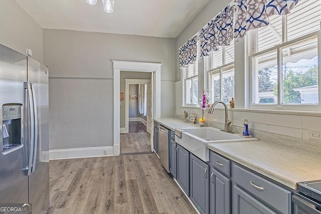 kitchen with stainless steel appliances, light wood-type flooring, gray cabinets, backsplash, and sink