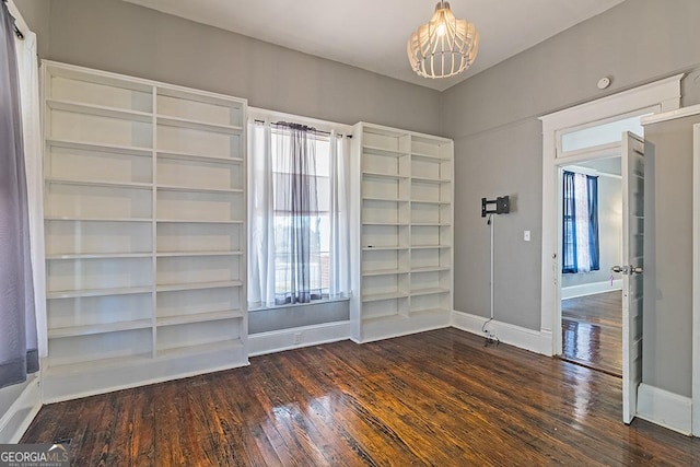 spare room with plenty of natural light, a notable chandelier, and dark hardwood / wood-style floors