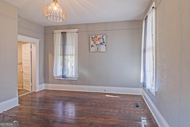 unfurnished room featuring an inviting chandelier and dark wood-type flooring