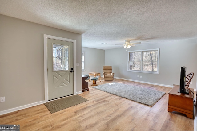 entryway featuring light wood-style floors, a ceiling fan, baseboards, and a textured ceiling