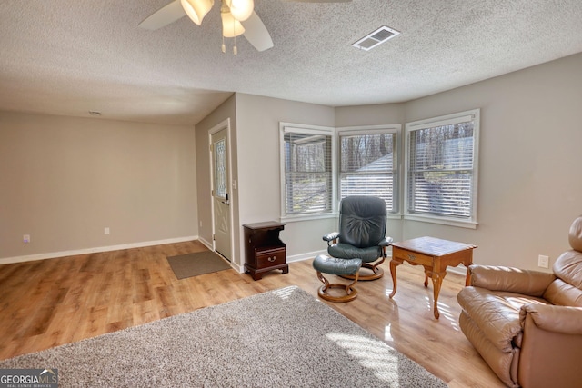 sitting room featuring light wood-type flooring, visible vents, a textured ceiling, and baseboards