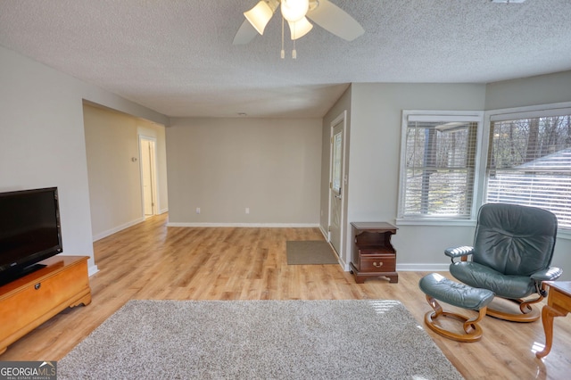 living room with a ceiling fan, a textured ceiling, baseboards, and wood finished floors