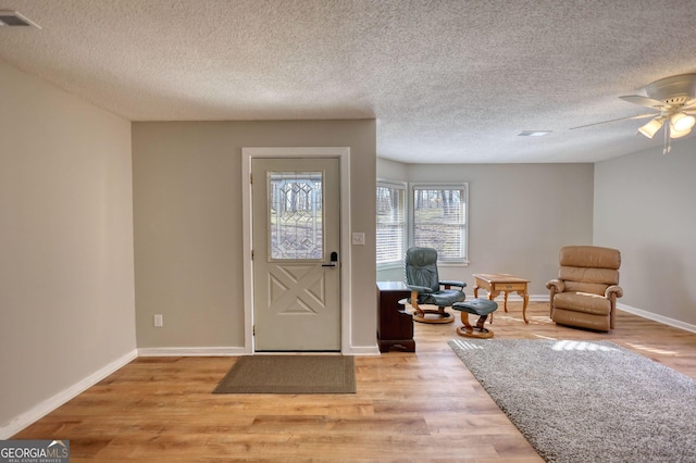 foyer featuring a textured ceiling, wood finished floors, a ceiling fan, visible vents, and baseboards