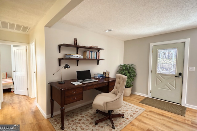 office area with a textured ceiling, baseboards, visible vents, and light wood-style floors