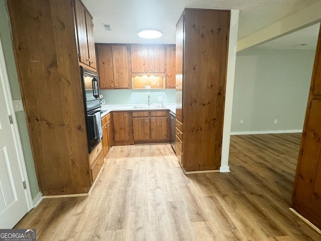 kitchen featuring light wood-type flooring, built in microwave, sink, dishwasher, and black oven